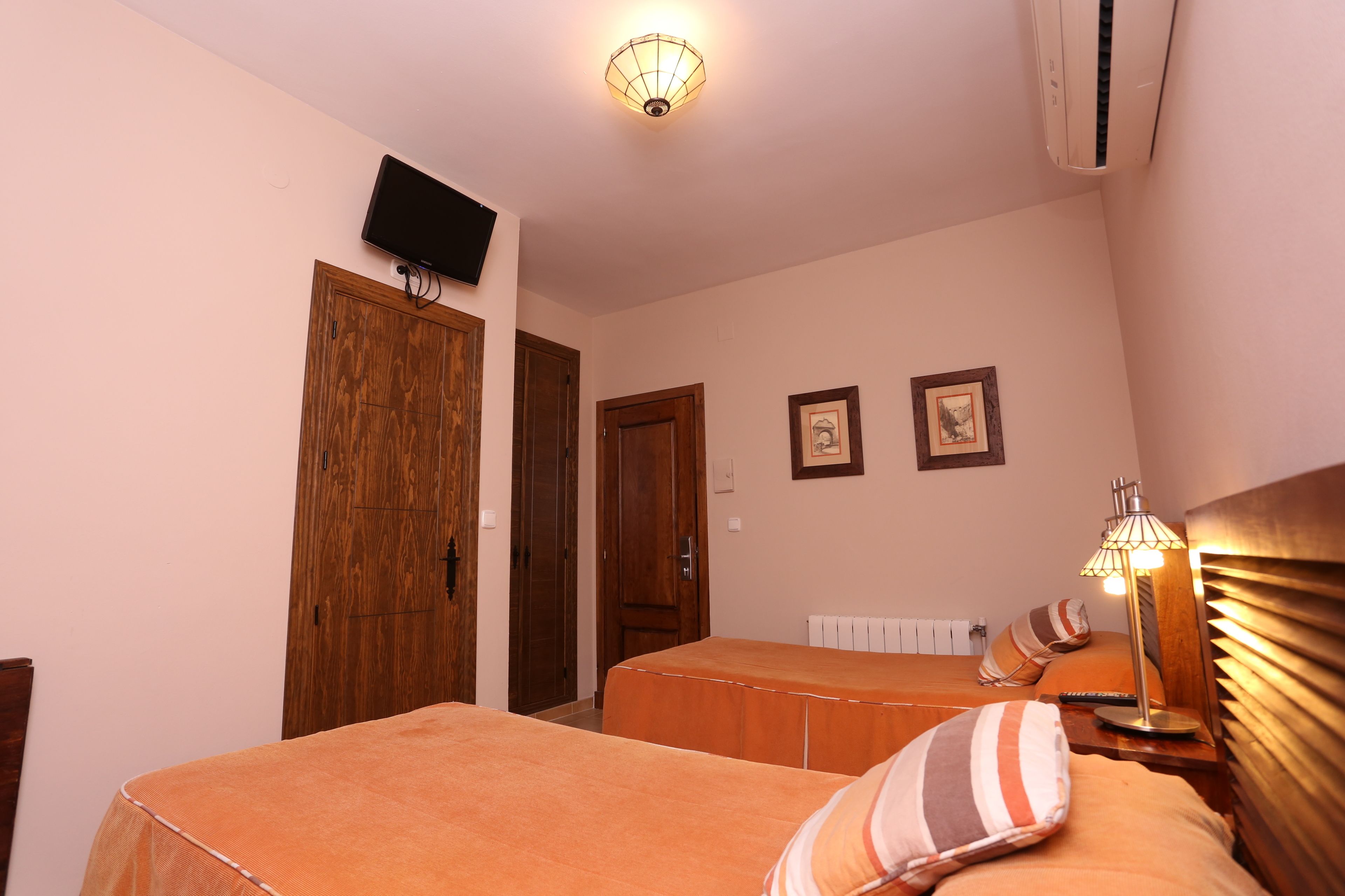 A bedroom with two beds, a television mounted on the wall, and a ceiling light fixture.