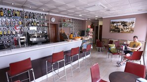 Zona de bar con barra, sillas rojas y un ordenador portátil sobre una mesa.