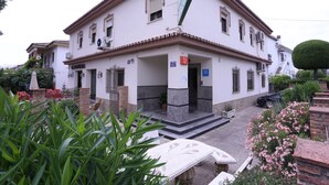 Un edificio de dos pisos con fachada blanca, múltiples ventanas y tejado de tejas.