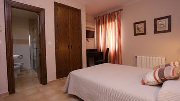 Comfortable room with a large bed, wardrobe, and desk, featuring a television and bathroom with a toilet and sink.
