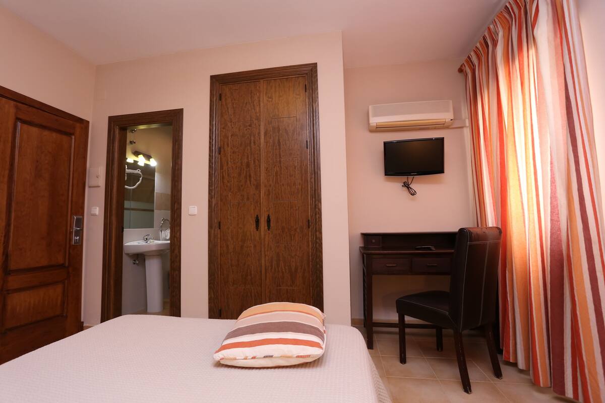 A hotel room with a bed, a desk, a chair, a TV, and a wardrobe.
