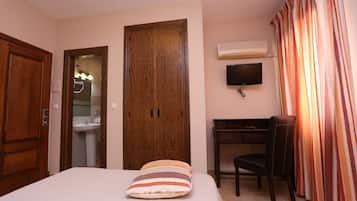 A hotel room with a bed, a desk, a chair, a TV, and a wardrobe.
