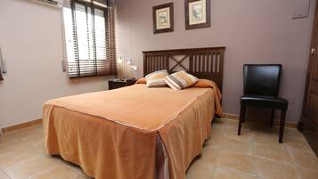 A bedroom with a large bed, a chair, a nightstand, and a window with blinds.