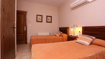 Habitación de hotel con dos camas, un armario de madera, un equipo de aire acondicionado y dos cuadros en la pared.