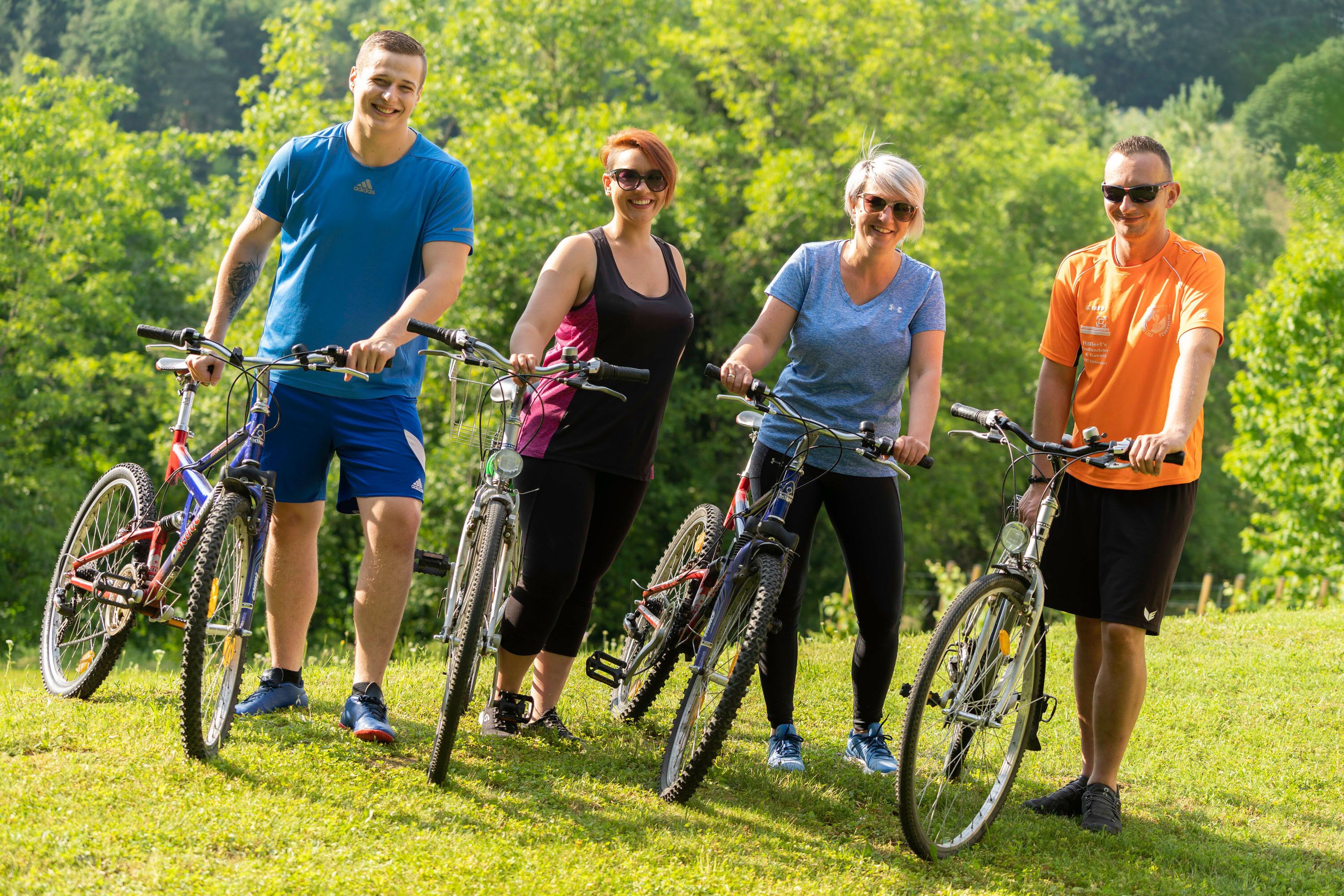 Cuatro personas de pie sobre césped con bicicletas, rodeadas de vegetación.