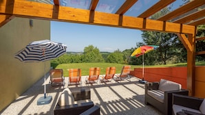 Un espacio de estar al aire libre techado, con mobiliario de mimbre y sombrillas a rayas, con vistas a un paisaje verde.