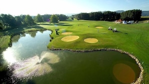 Un campo de golf con un estanque, búnkeres de arena y un club de campo al fondo.