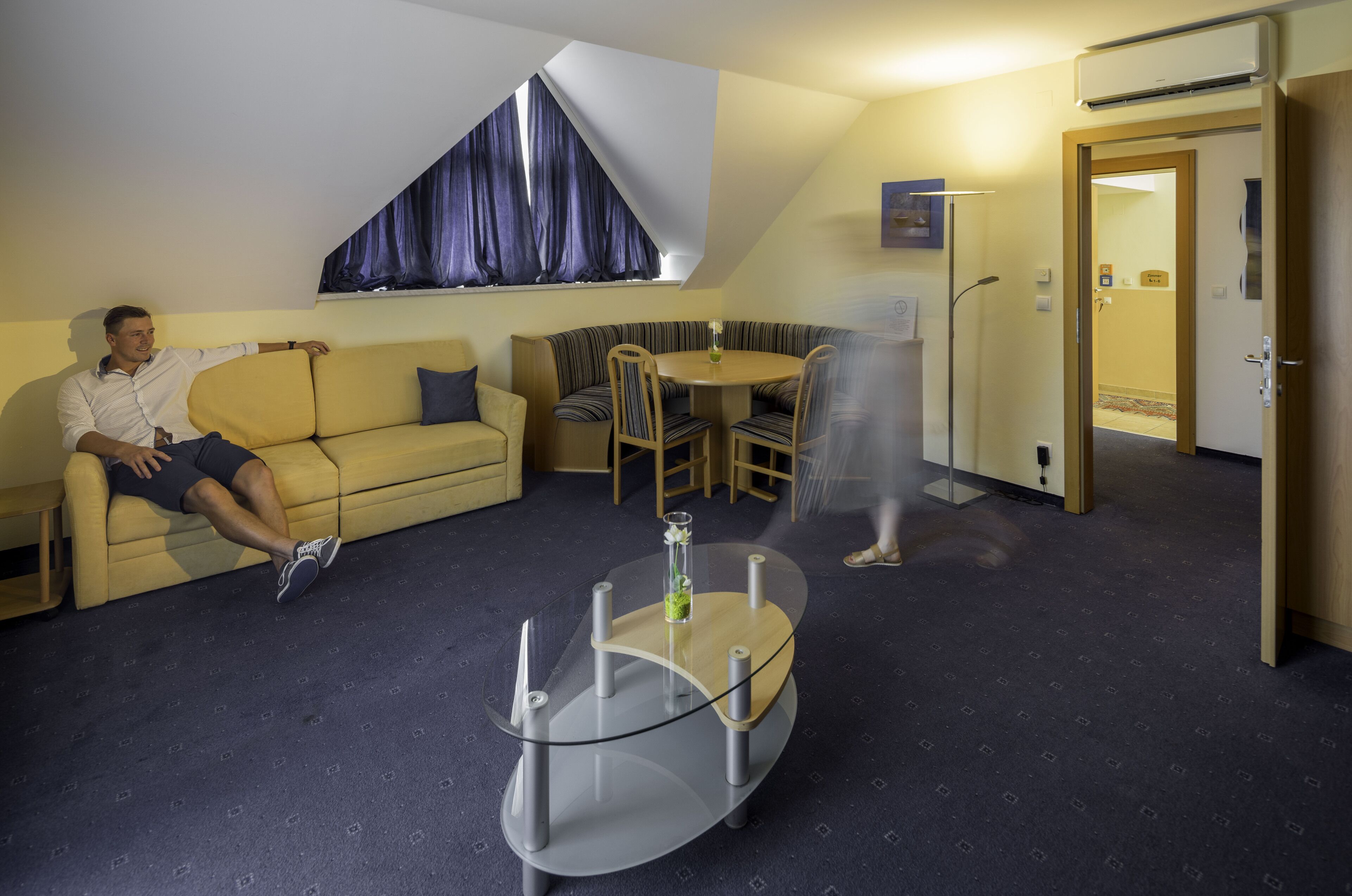 Ein modernes Hotelzimmer mit einer Couch, einem Glastisch und einem Essbereich.