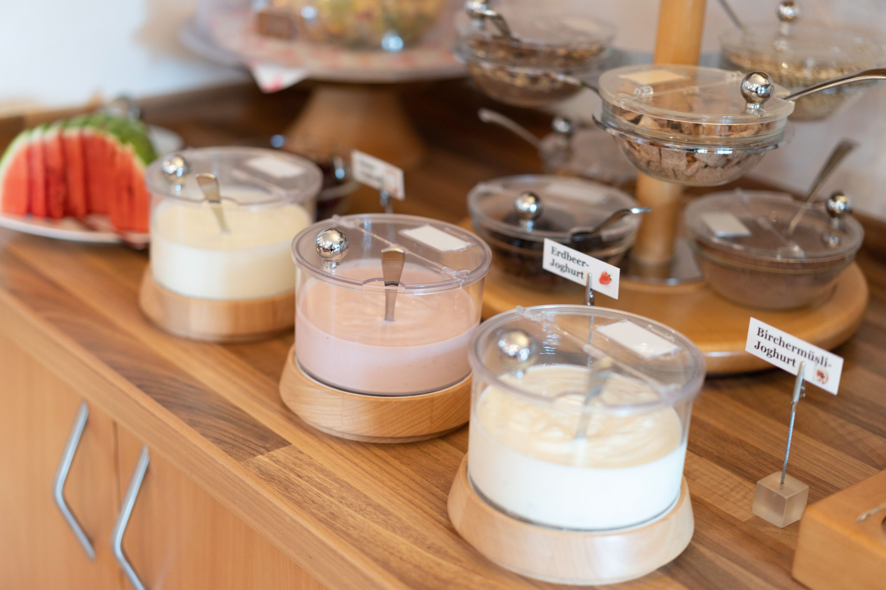 Una mesa de buffet con varios recipientes de yogur etiquetados en distintos idiomas.