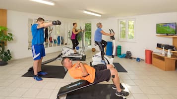 Un gimnasio con equipo de ejercicio, un televisor y un espejo.