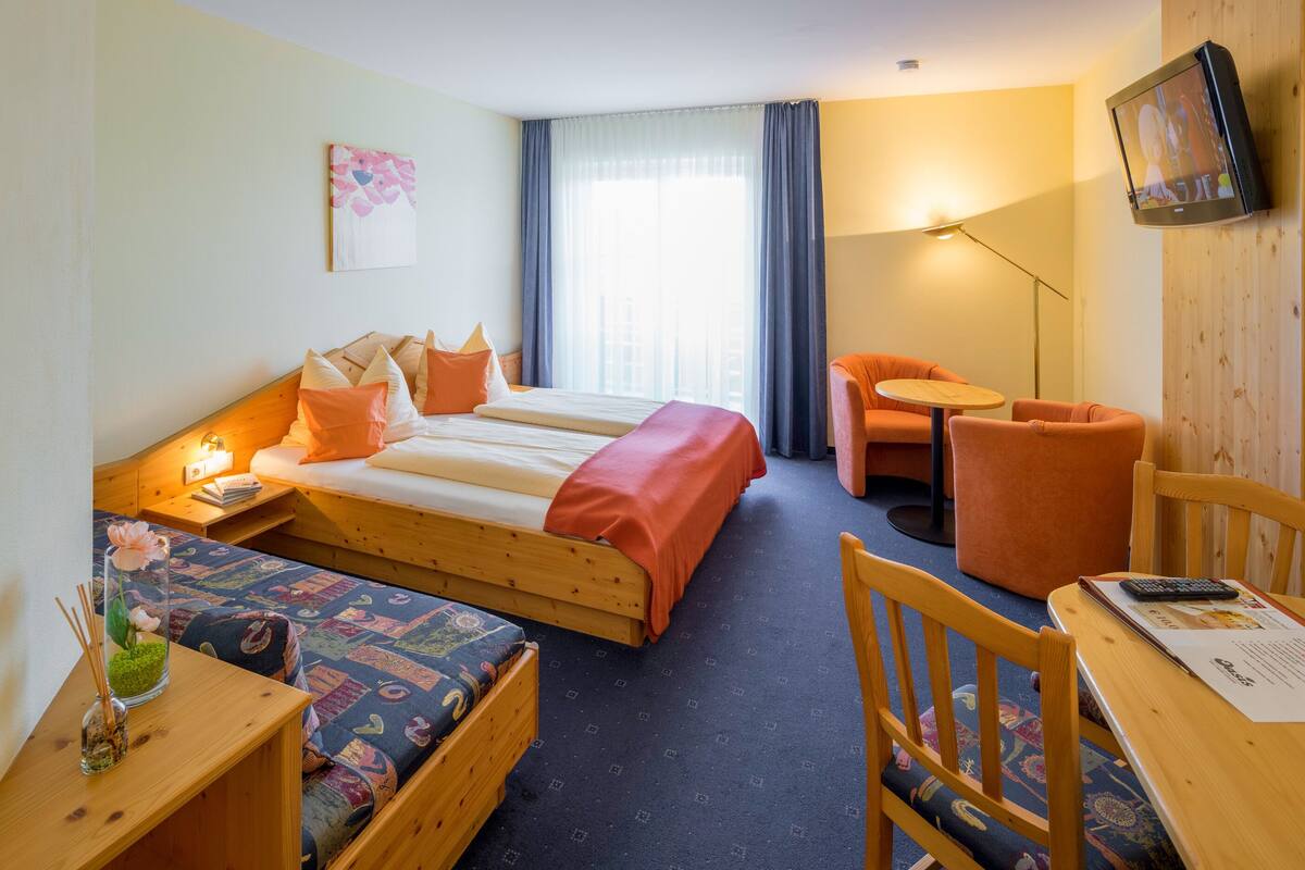 Une chambre d’hôtel avec deux lits, un bureau, une chaise, une télévision et une fenêtre avec des rideaux.