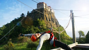 A person bungee jumping with a rope attached to a wooden platform, overlooking a castle on a hill.