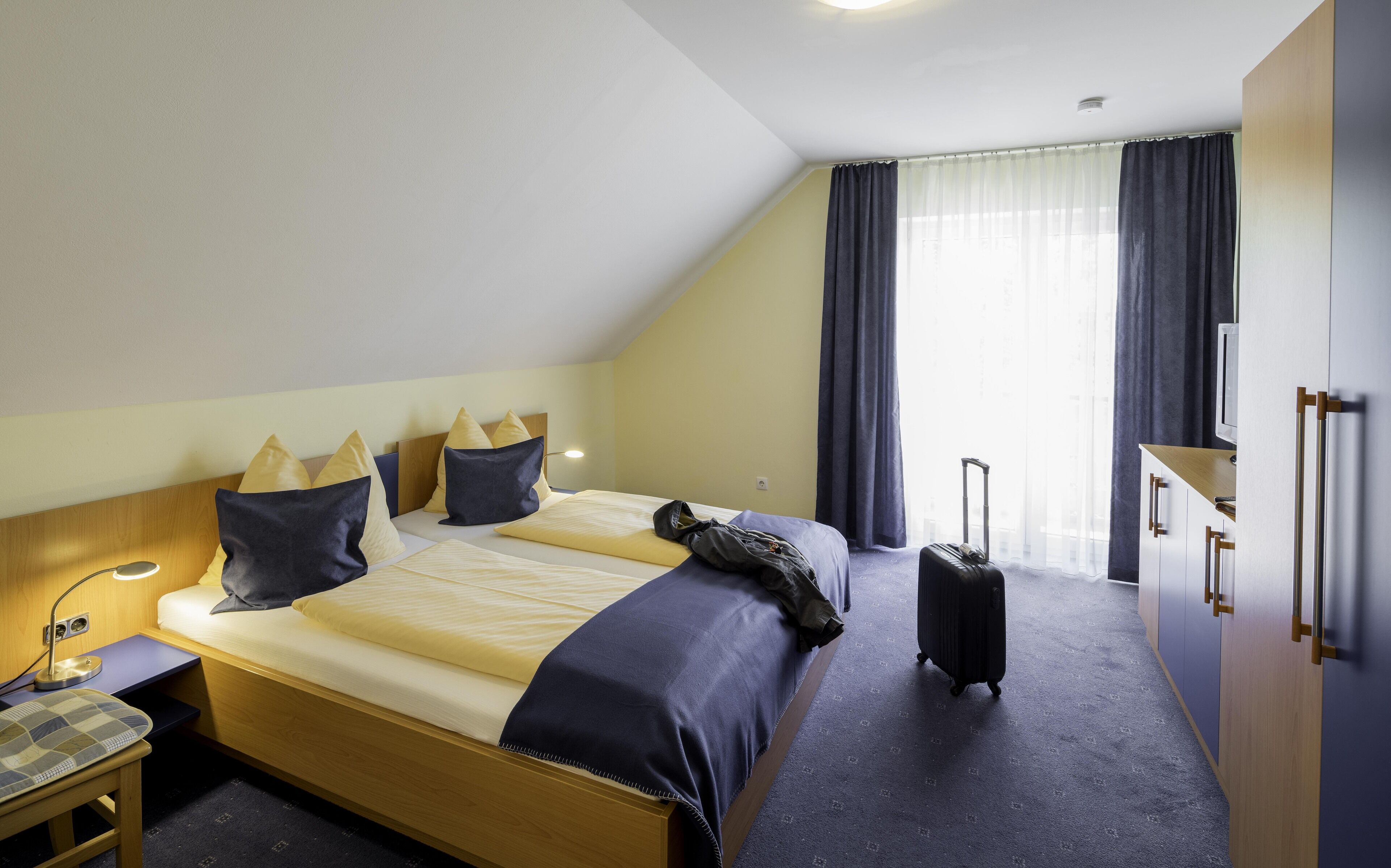 A hotel room with a bed, a desk, a suitcase, and a wardrobe.