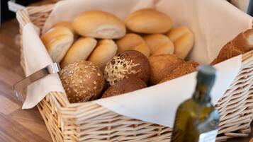 A wicker basket filled with various types of bread, including rolls and seeded buns, placed on a wooden table.