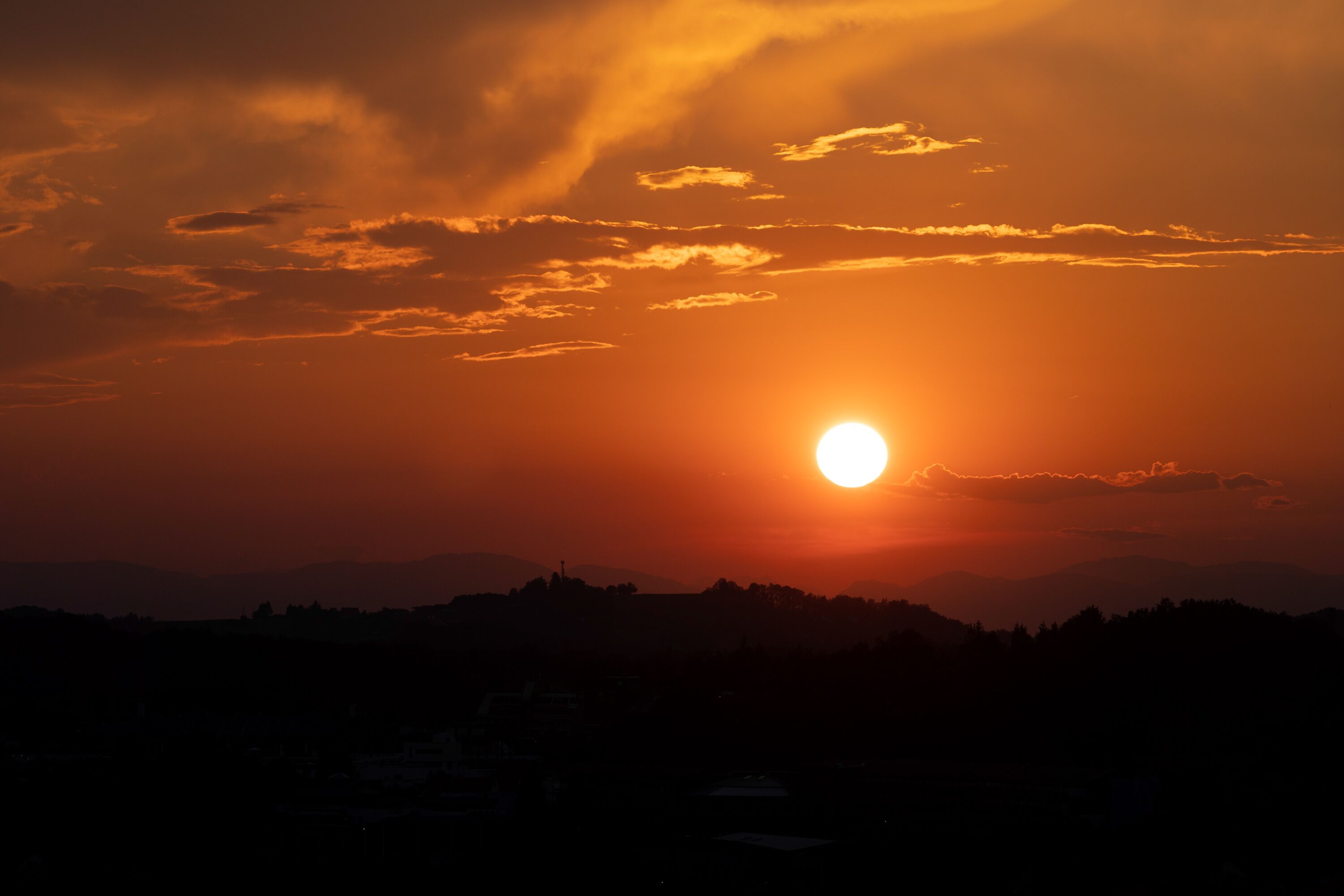 A sunset over a mountainous landscape with silhouettes of buildings.
