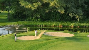 Un campo de golf con búnkeres de arena, un estanque y árboles al fondo.