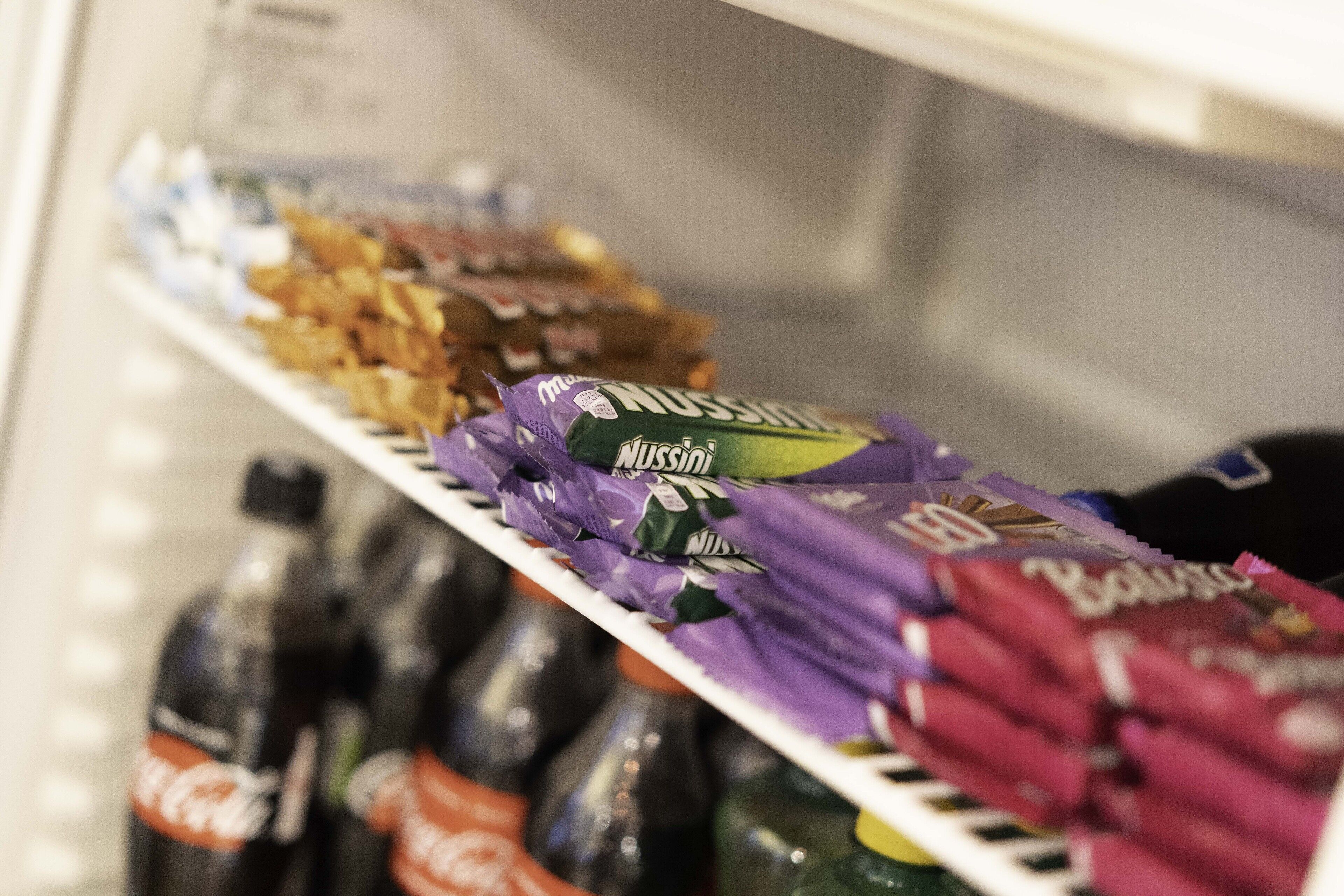 Ett kylskåp fyllt med olika sorters matvaror, inklusive flaskor med läsk och förpackningar med snacks.