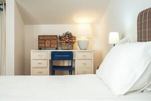 Habitación de hotel con cama, escritorio con cajones, silla, lámpara y una cesta decorativa con flores.