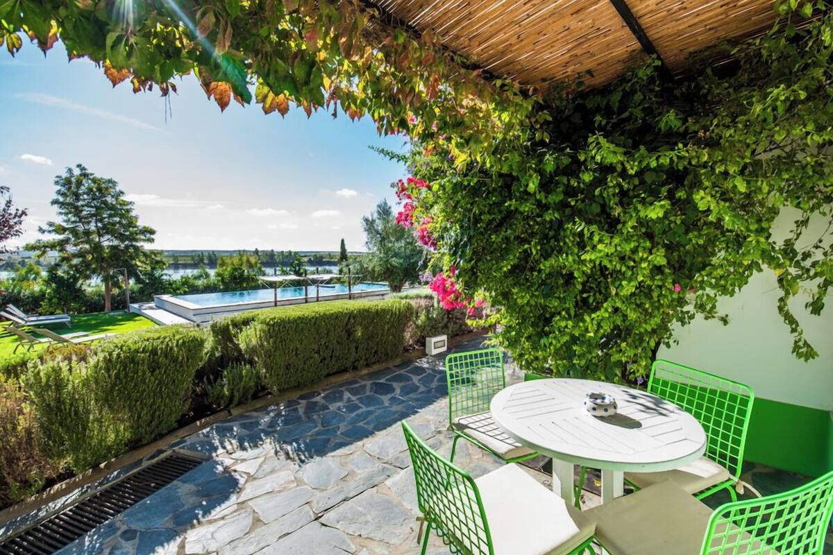 Une terrasse avec un sol en pierre, des chaises en métal vert, une table blanche et une vue sur une piscine.