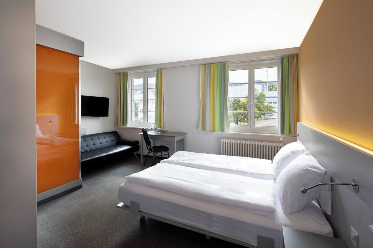 A hotel room with a bed, a desk, a chair, a TV, and a window with curtains.
