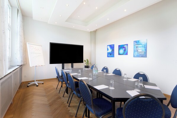 A conference room with a long table, blue chairs, a whiteboard, and a flat-screen TV.