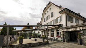 A building with a covered patio area, stone flooring, and potted plants. - Hotel & Gasthaus die Perle (Perlen)