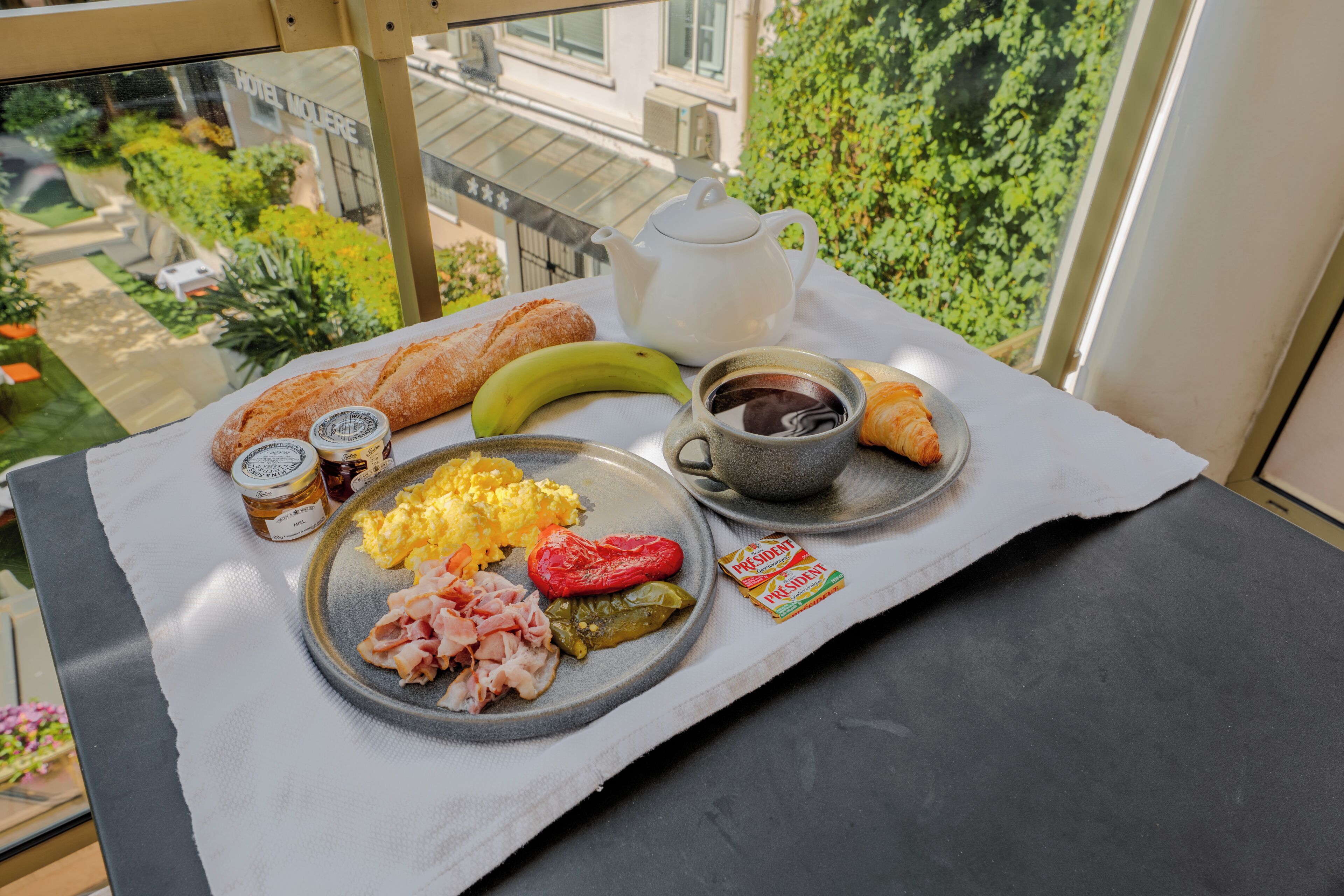 A breakfast setup with croissants, a banana, scrambled eggs, ham, and a croissant on a tray.