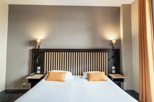 A hotel room with a large bed, two bedside tables, a headboard with vertical slats, and two wall-mounted lamps.