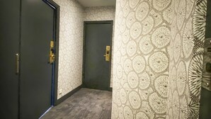 A hallway with patterned wallpaper, dark wooden flooring, and two doors with brass handles. - Hotel Molière (Cannes)