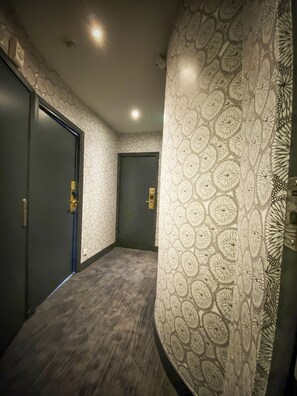 Un pasillo con papel tapiz estampado, suelo de madera oscura y dos puertas con manijas de latón.