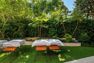 Een terras met tafels en stoelen, omgeven door weelderige beplanting en bomen.