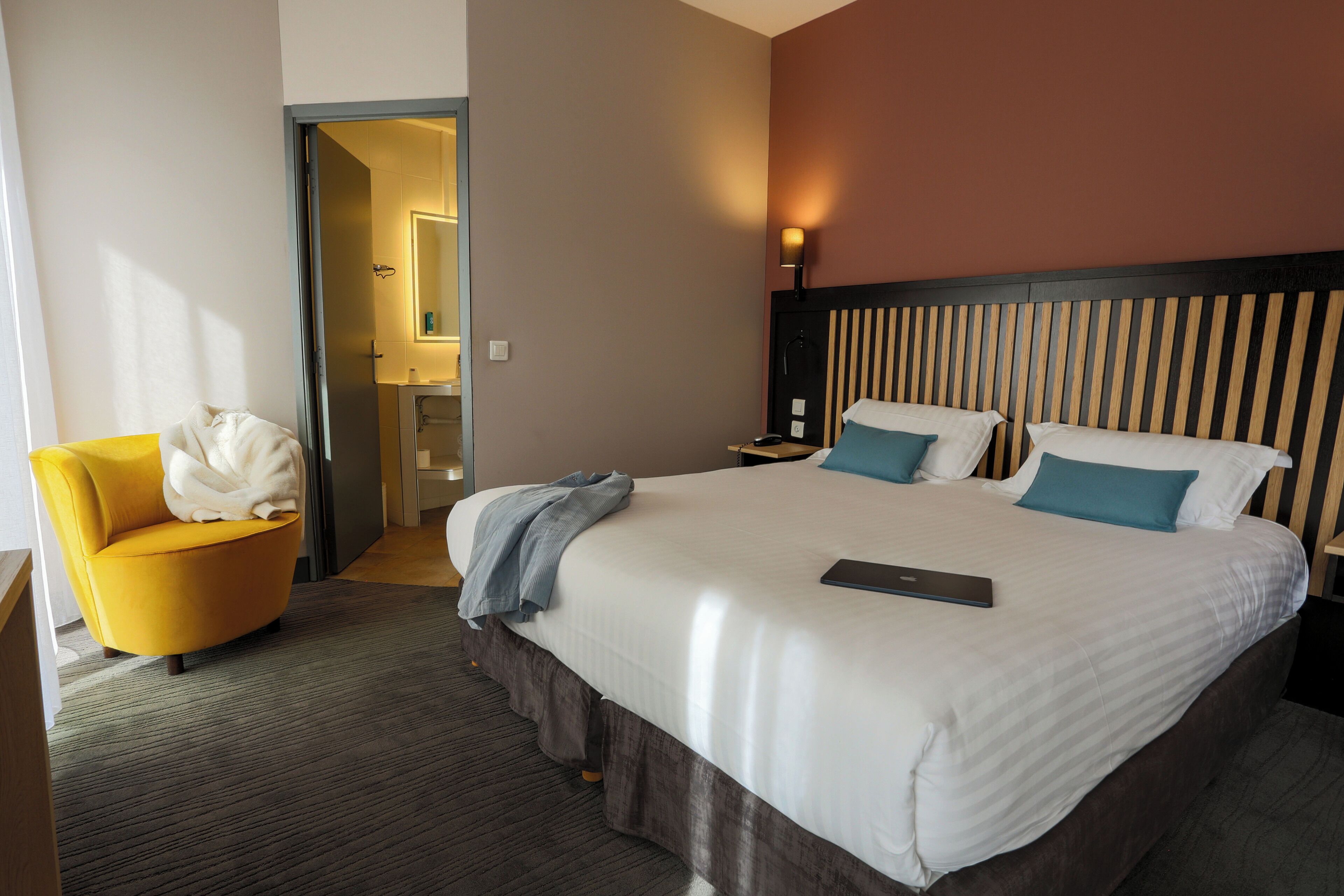 A hotel room with a bed, a chair, a bedside table, and a lamp.