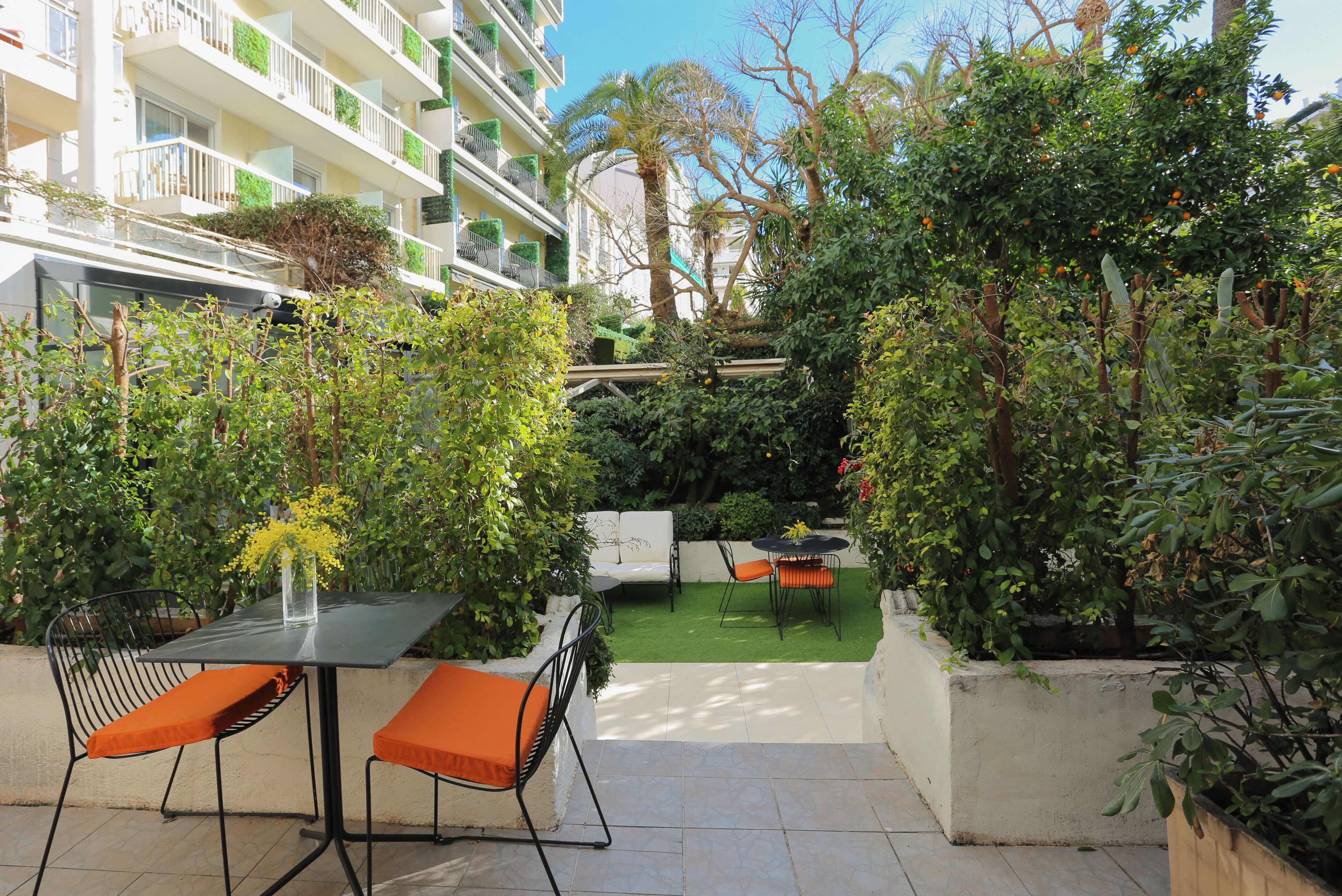 An outdoor patio area with a table and chairs, surrounded by lush greenery and a view of a multi-story building.
