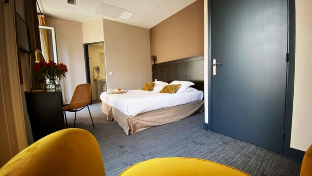 A hotel room with a bed, a desk with a lamp, a chair, and a door. - Hotel Molière (Cannes)