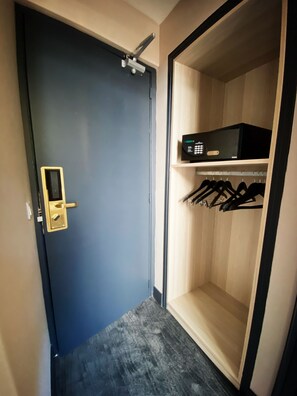 Una habitación con una puerta azul oscuro, un pequeño estante con un microondas y un perchero con ganchos negros.