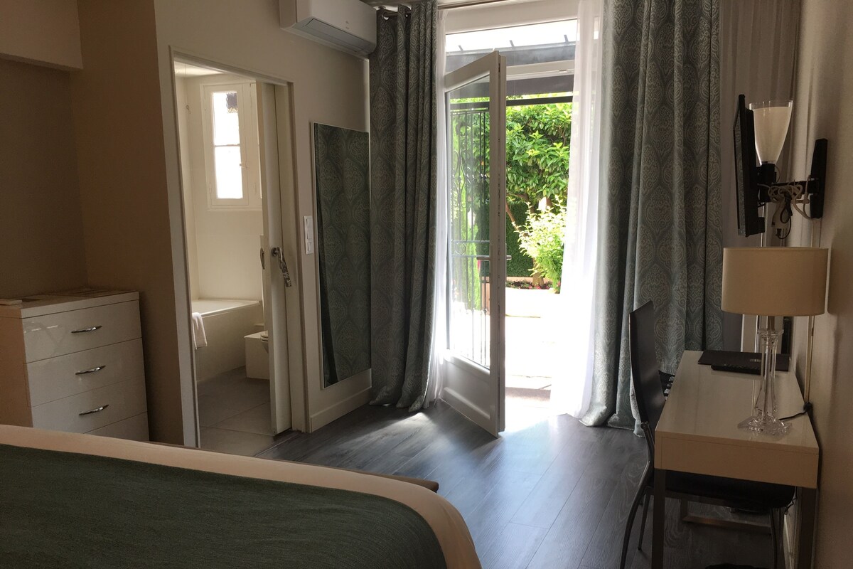 Un dormitorio con cama, escritorio, silla, lámpara y vistas al exterior a través de una puerta.