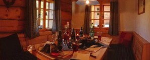 Ein Holzblockhaus-Interieur mit einem Esstisch, der für zwei Personen gedeckt ist, mit verschiedenen Flaschen und Gläsern.