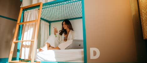 A bunk bed with a ladder, a laptop, and a person using a smartphone.