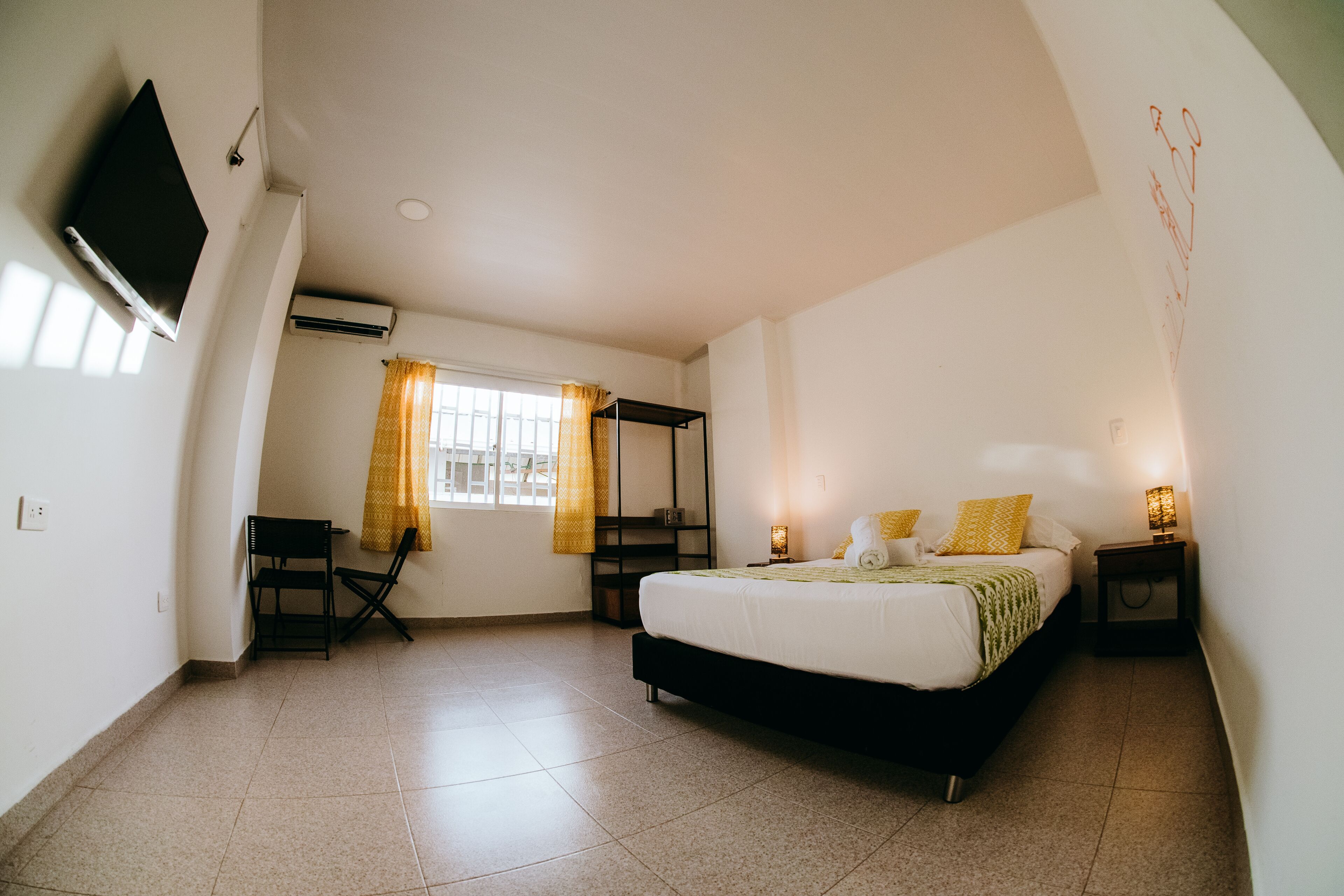 A bedroom with a bed, bedside tables, a TV, and a window with curtains.