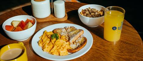 A breakfast table with scrambled eggs, toast, fruit, granola, and a glass of orange juice.