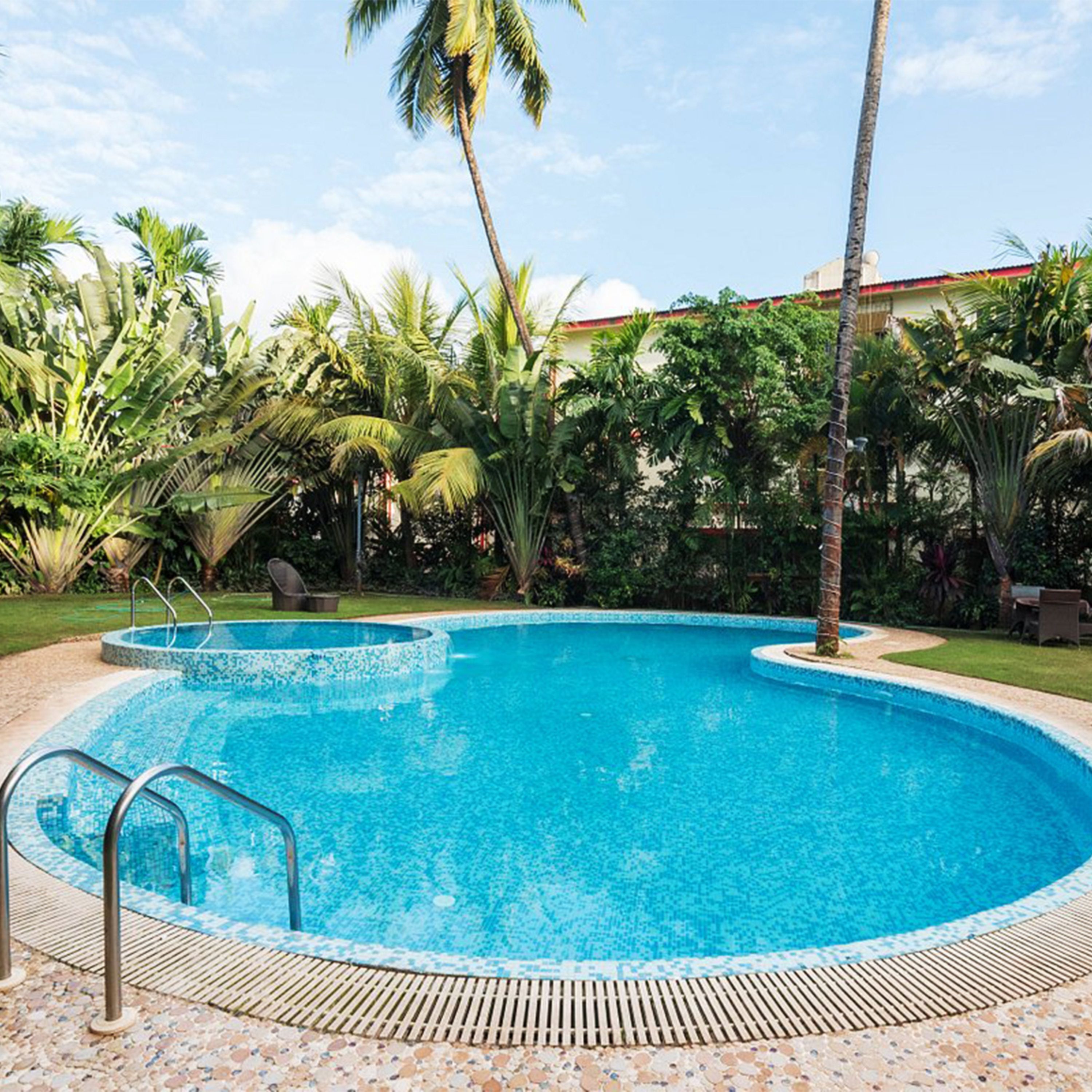 A swimming pool with a tiled edge, surrounded by palm trees and other tropical plants.
