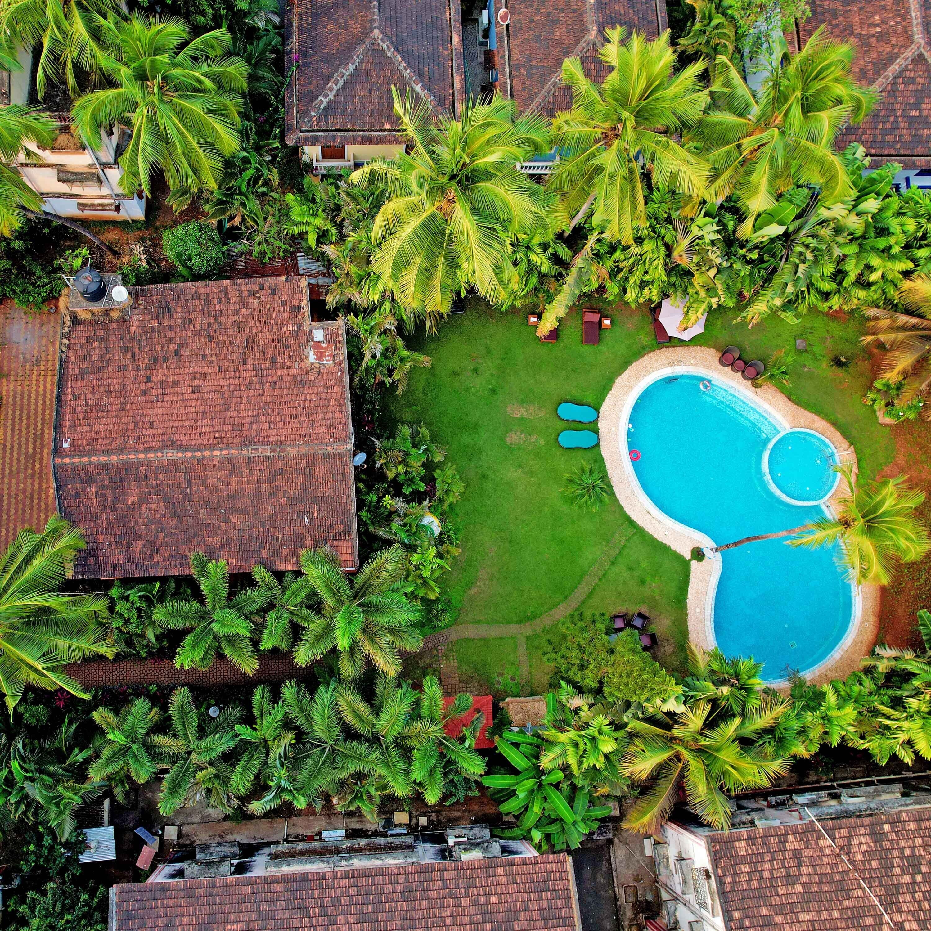 Vue aérienne d’un quartier résidentiel avec une piscine entourée d’une végétation luxuriante et de palmiers.