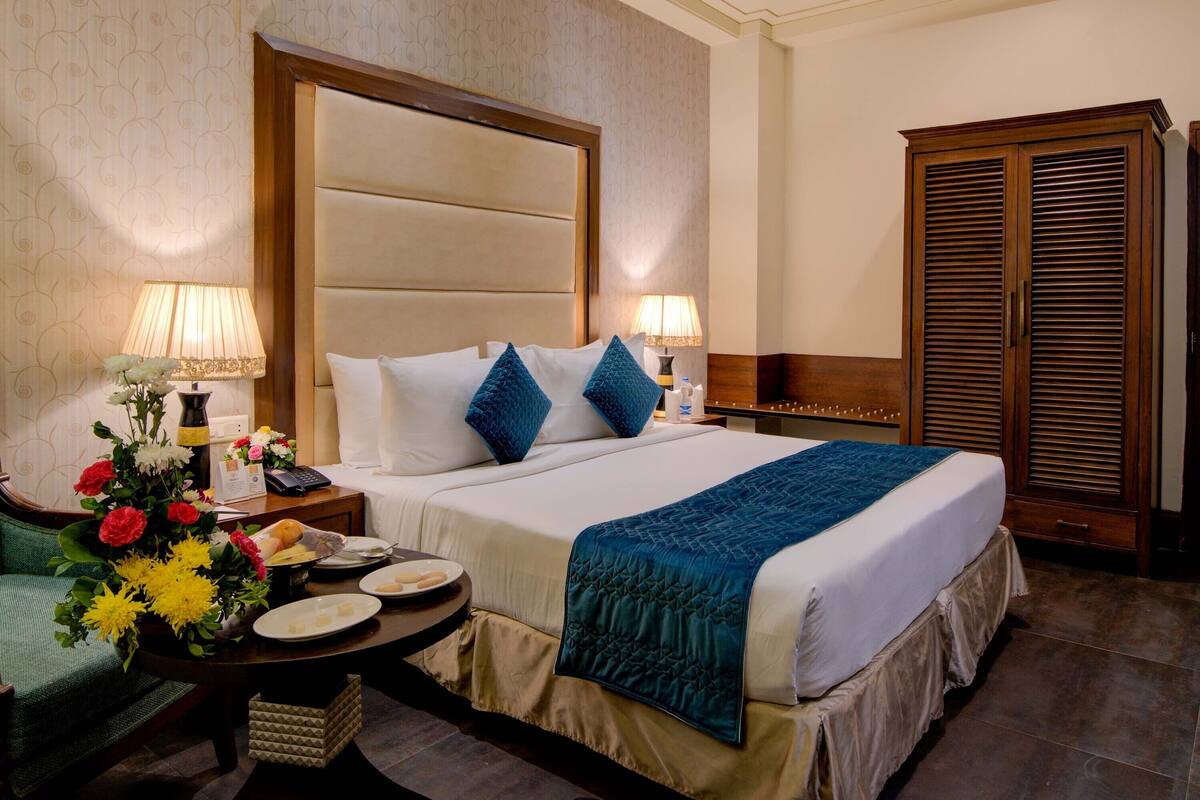 A hotel room with a large bed, two bedside tables with lamps, a wooden wardrobe, and a ceiling fan.