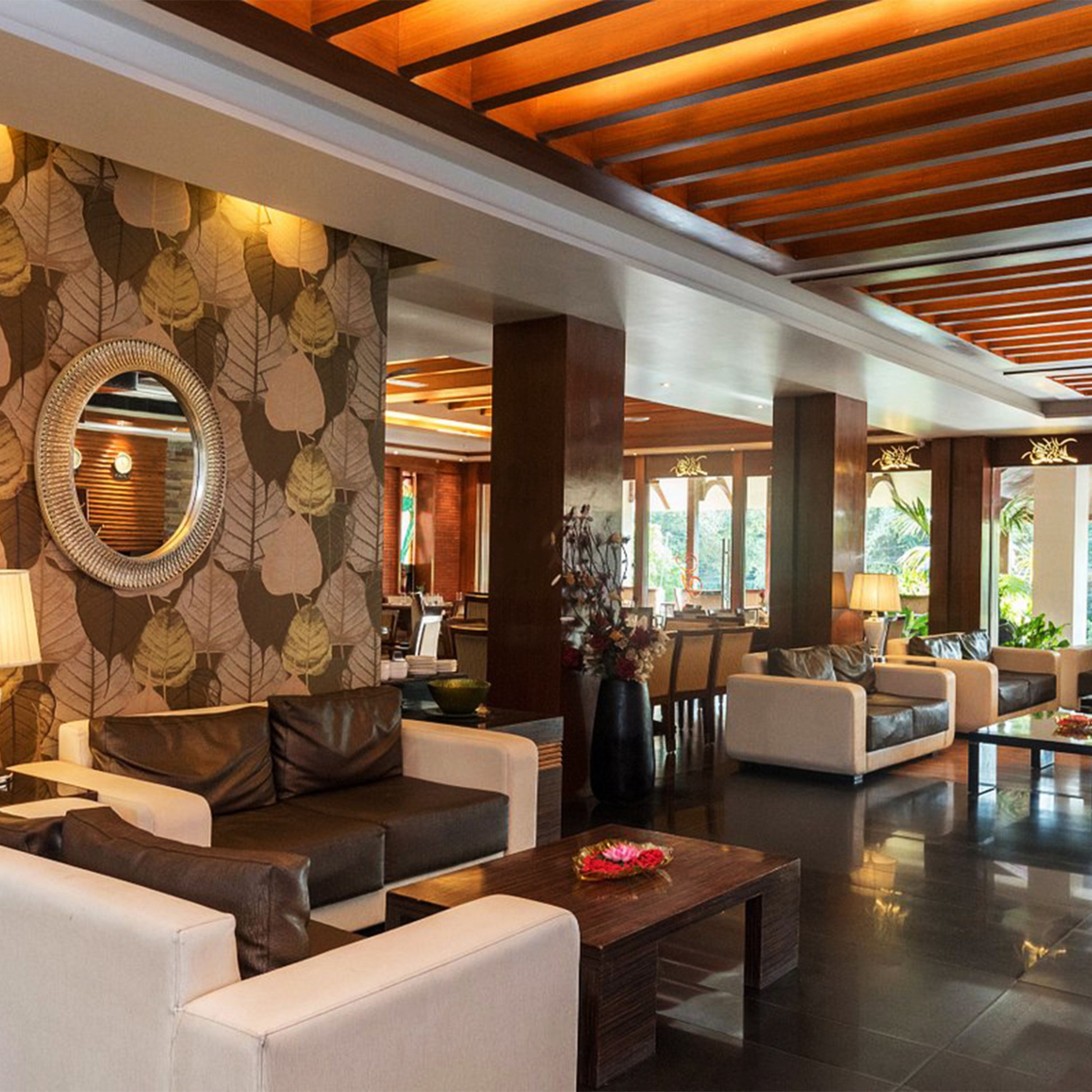 A spacious lobby with a modern design, featuring leather sofas, a wooden coffee table, and a large mirror with a leaf pattern on the wall.