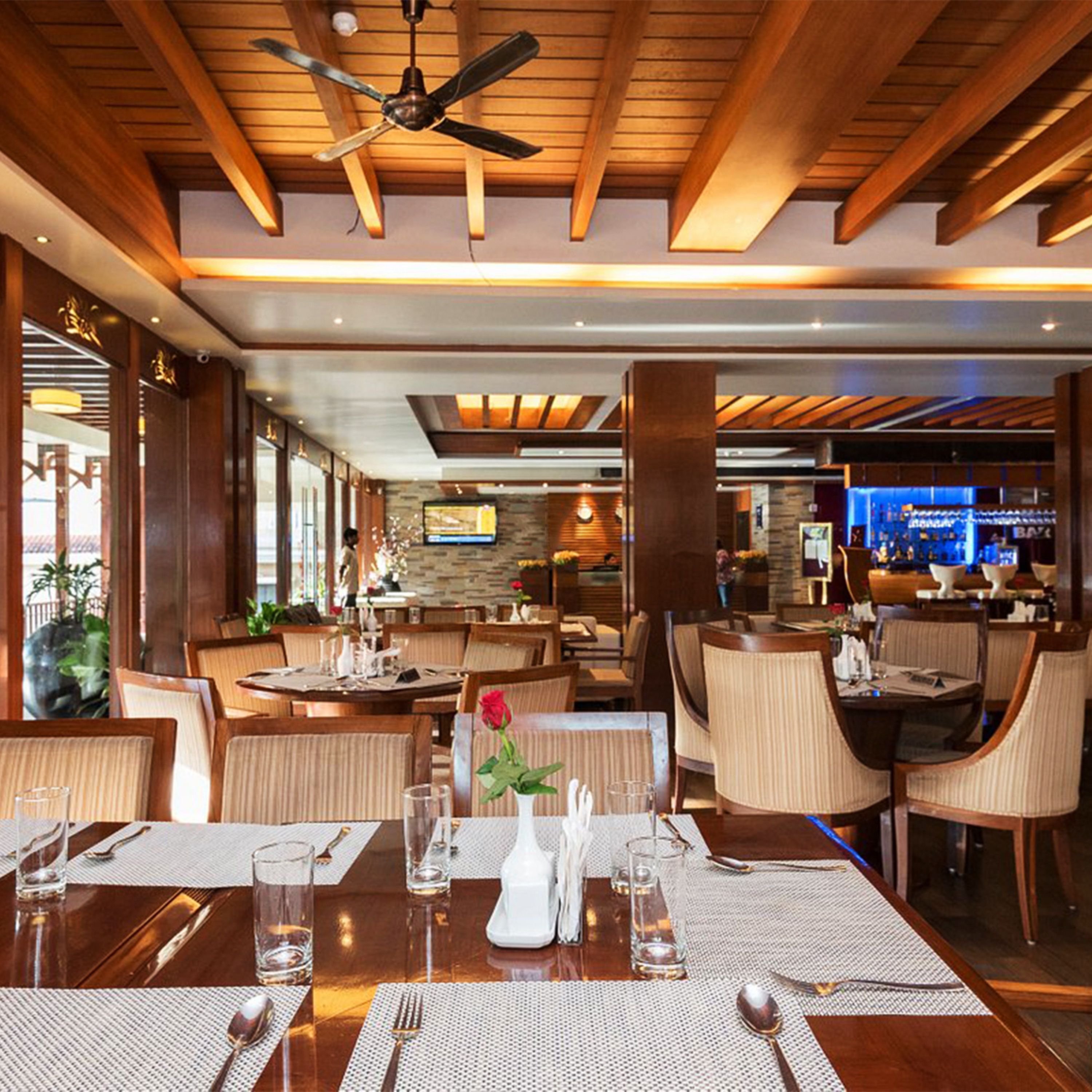 A restaurant with wooden ceiling beams, multiple dining tables with chairs, a bar area, and a television screen.