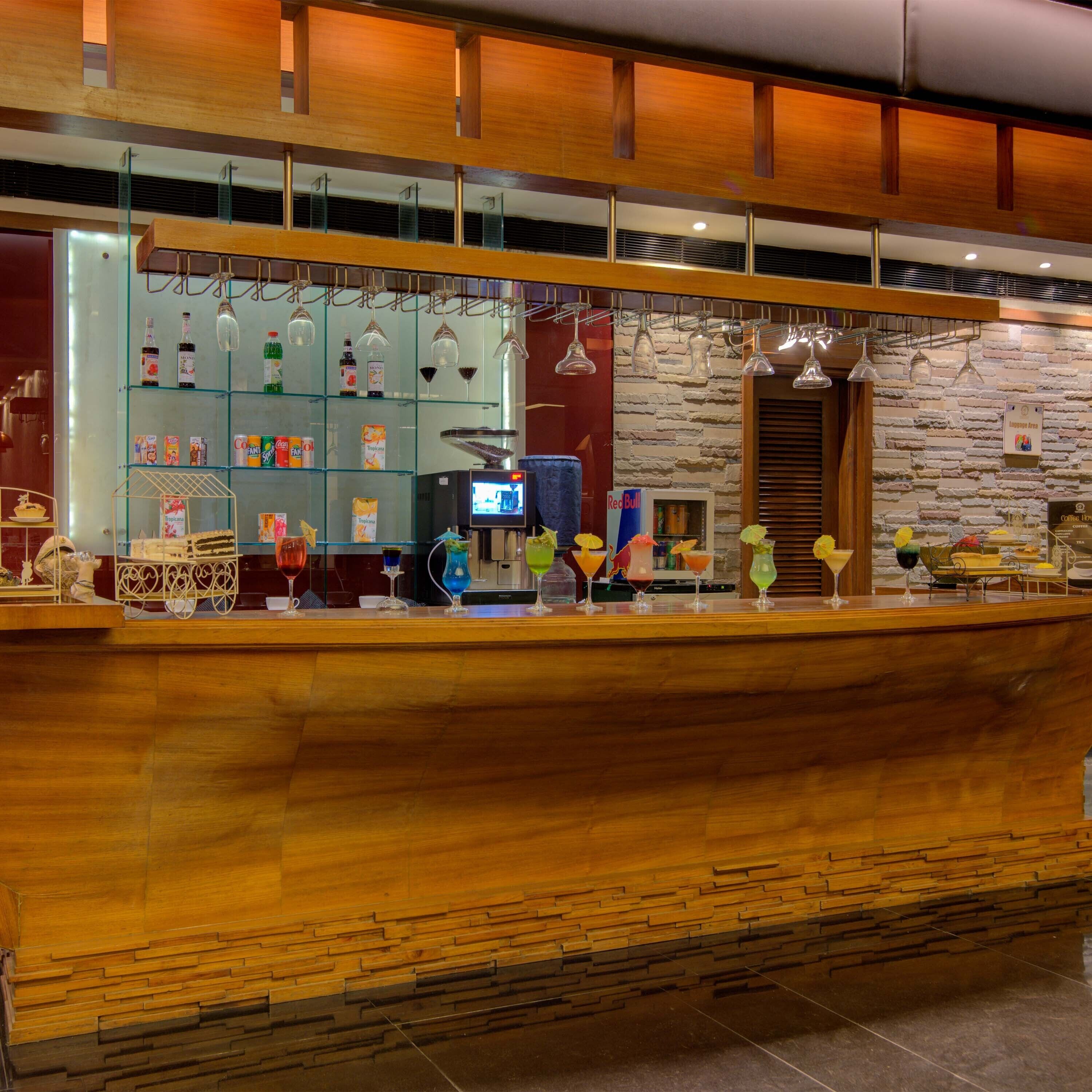 A bar area with a wooden counter, shelves with beverages, and hanging lights.