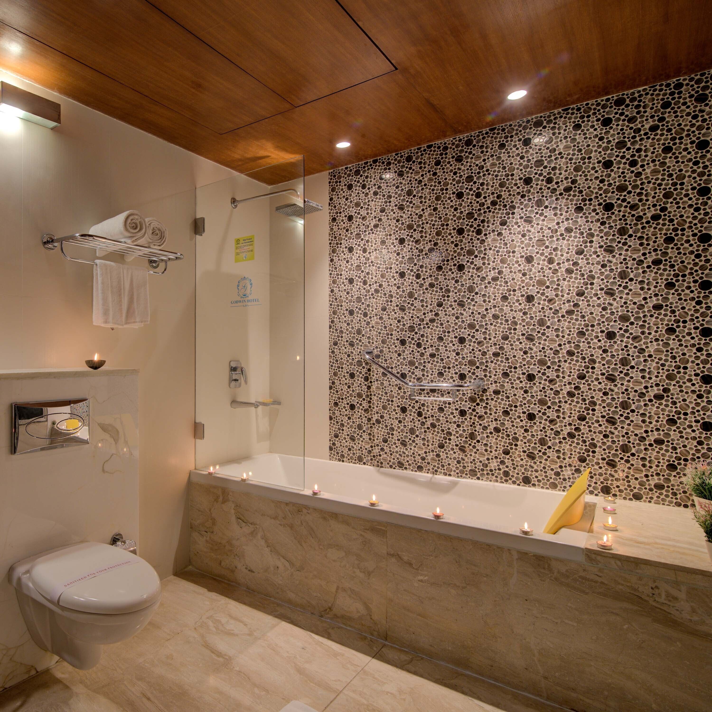 A modern bathroom with a marble sink, a bathtub with candles, a glass shower enclosure, and a wooden ceiling.