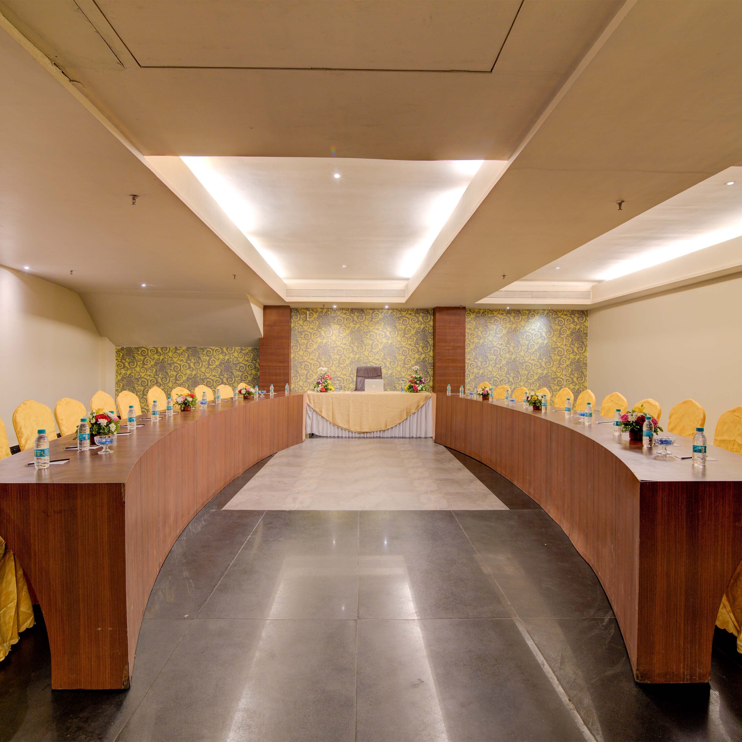 Une salle de conférence avec une longue table, des chaises jaunes et des centres de table ornés de motifs floraux.