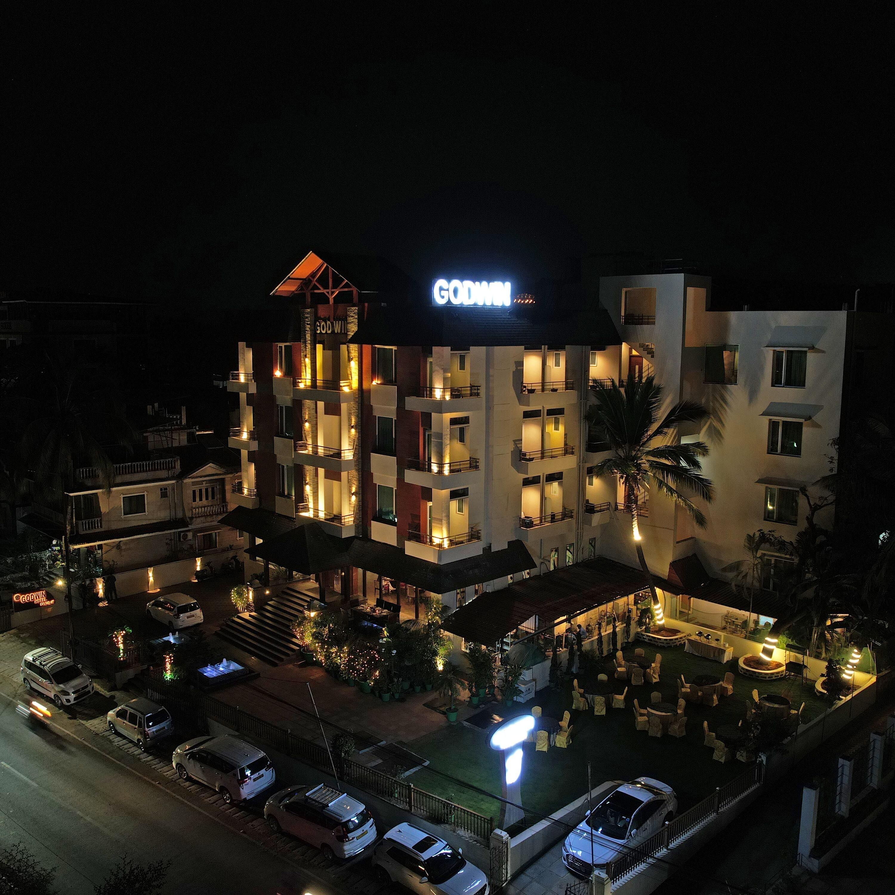 A multi-story hotel with a prominent 'GODWIN' sign, outdoor seating, and a well-lit entrance.