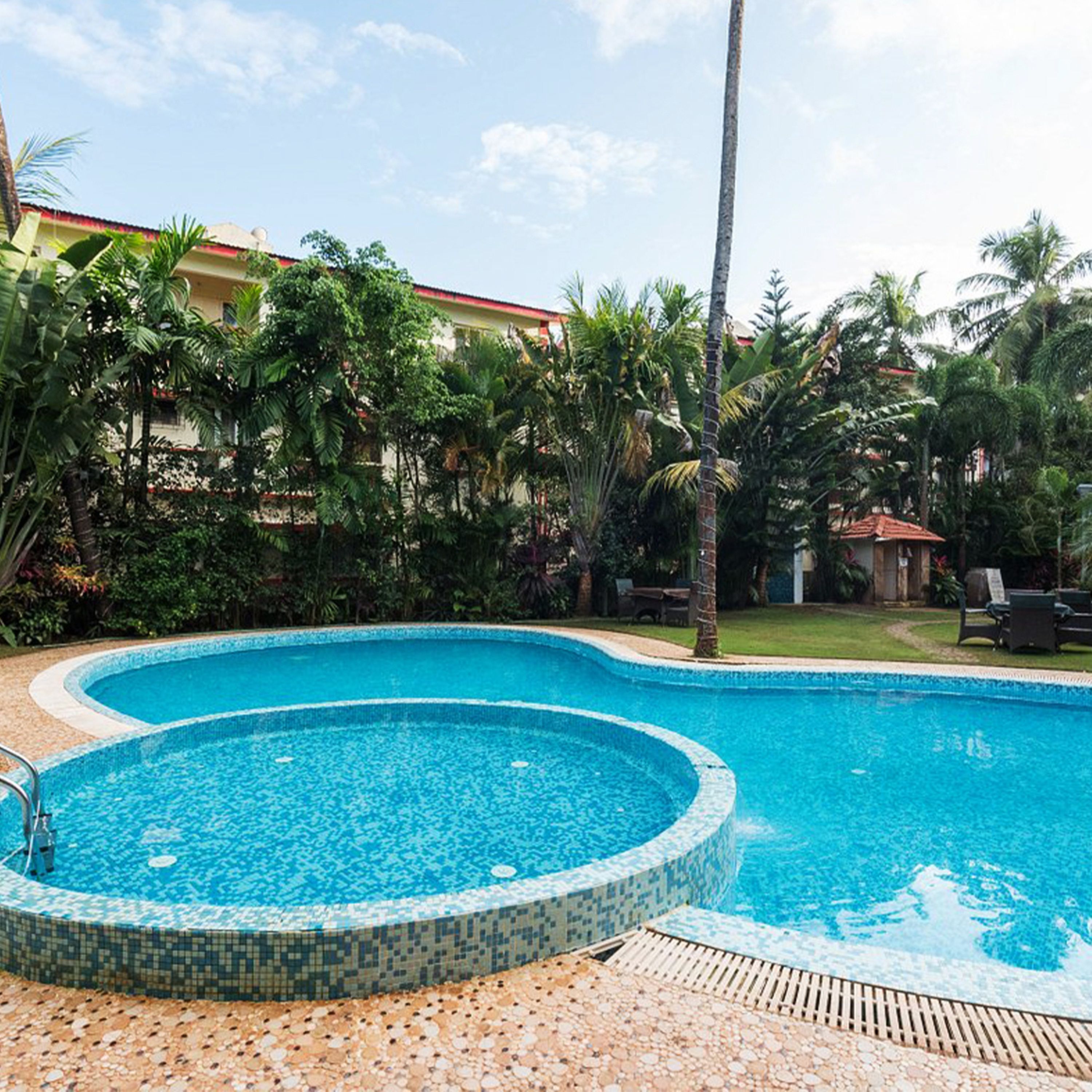 A swimming pool with a tiled edge, surrounded by palm trees and a building with a red roof.